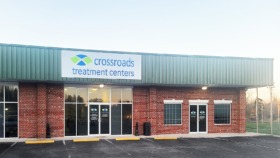 Exterior front view of treatment center building with red brick facade, green metal roof, and Crossroads Treatment Centers signage