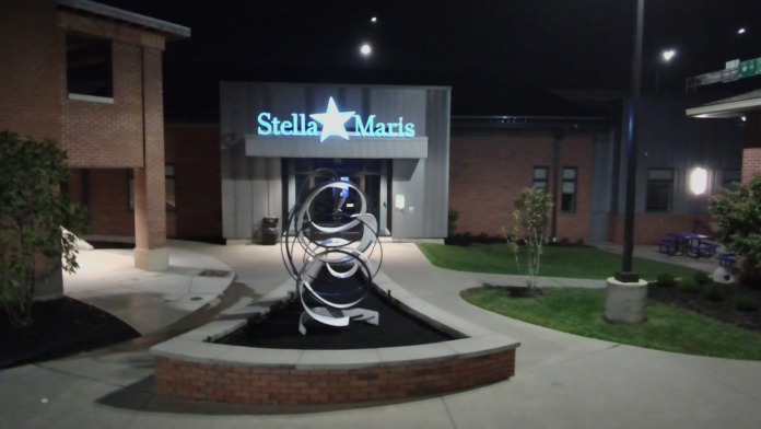 Exterior nighttime view of Stella Maris facility entrance with illuminated signage, landscaping, and sculpture