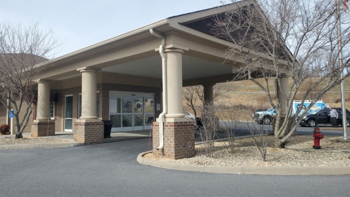 Exterior view of clinic entrance with brick construction, covered portico with columns, and parking area visible