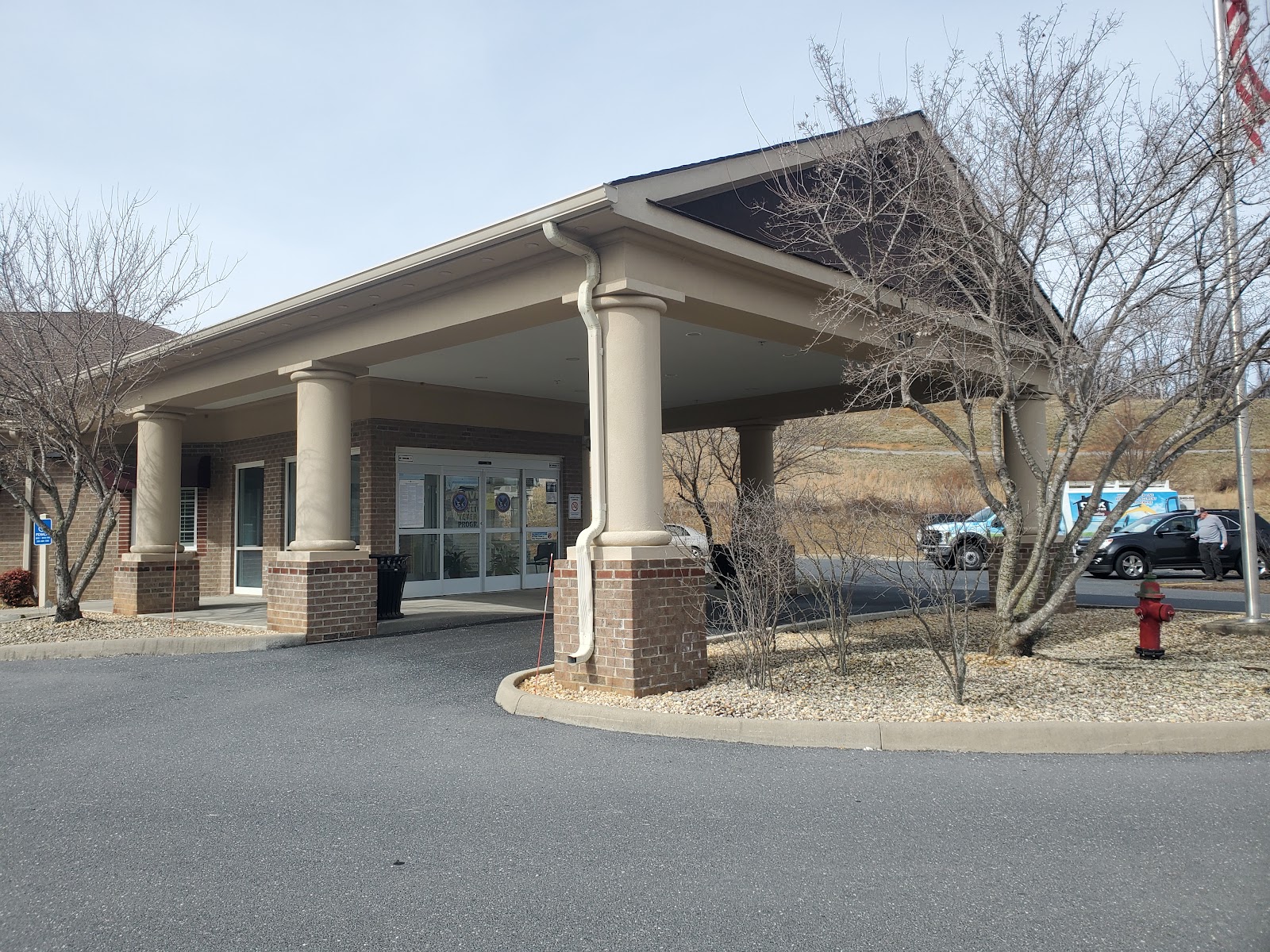 Exterior view of clinic entrance with brick construction, covered portico with columns, and parking area visible