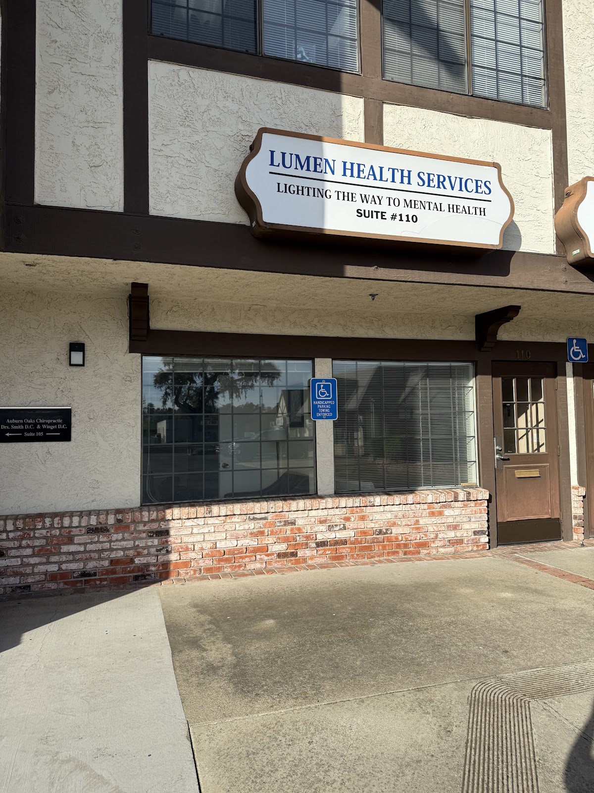 Exterior storefront showing Lumen Health Services main entrance with prominent signage, brick base, and accessible parking indicator
