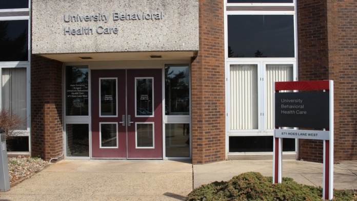 Exterior view of University Behavioral Health Care main entrance with brick facade, red entry doors, and facility signage on white panel
