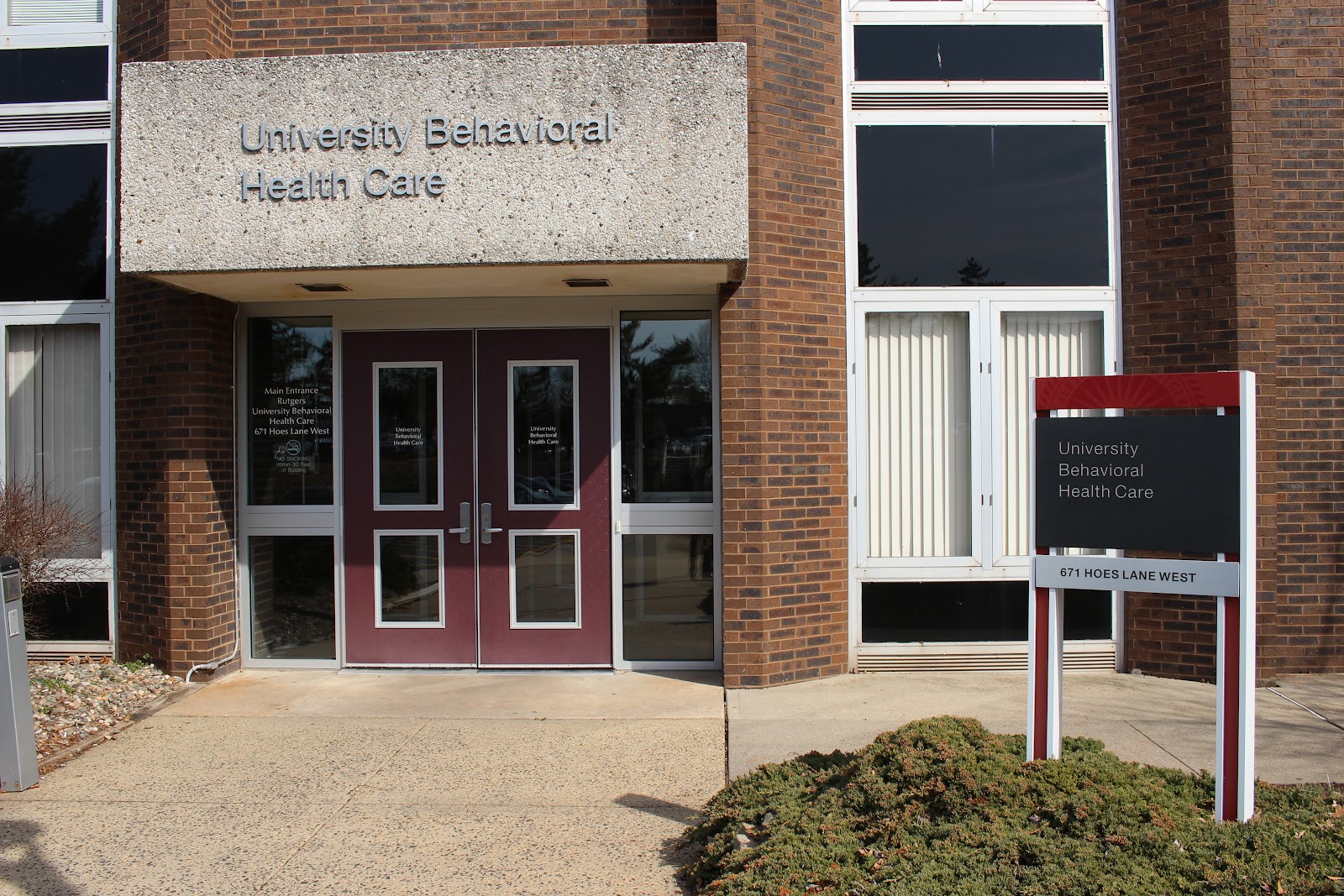 Exterior view of University Behavioral Health Care main entrance with brick facade, red entry doors, and facility signage on white panel