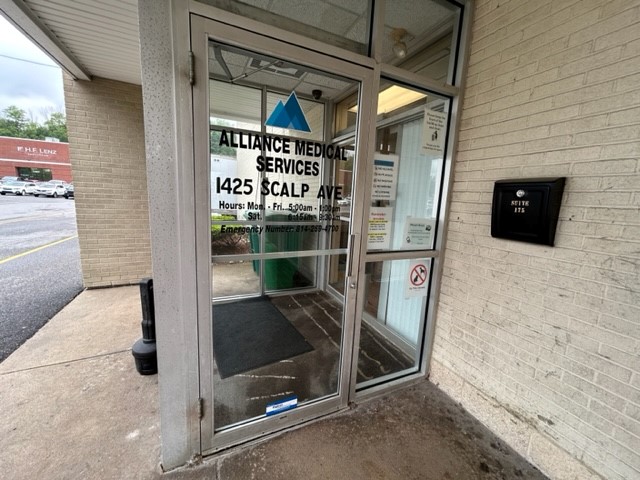 Exterior entrance showing Alliance Medical Services signage at 1425 Scalp Avenue with glass doors and brick facade