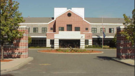 Exterior view of treatment center showing brick and white front facade with central entrance, landscaped grounds, and driveway