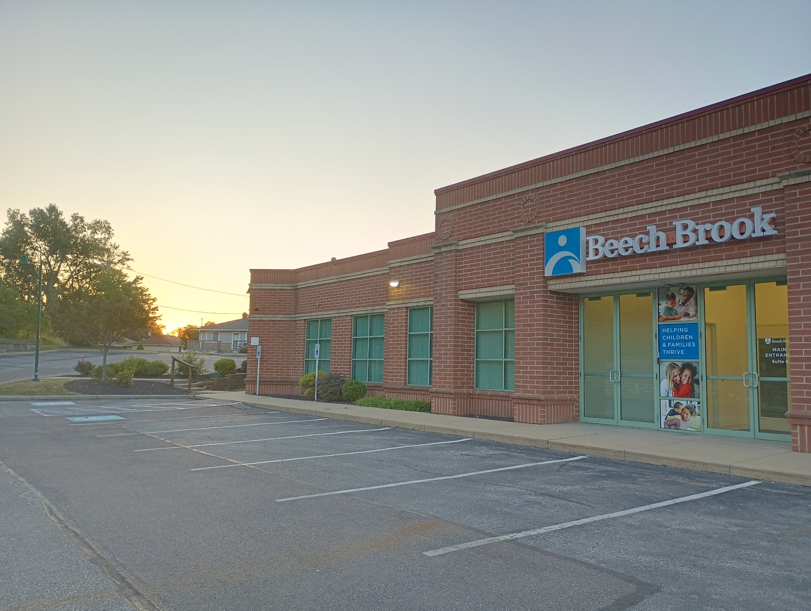 Exterior view of Beech Brook facility showing brick building with teal entrance doors, Beech Brook signage, and parking area at sunset