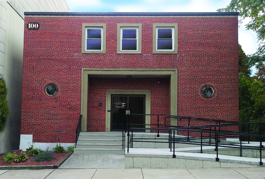 Exterior view of brick building entrance with address number 100, metal railings, and glass doors