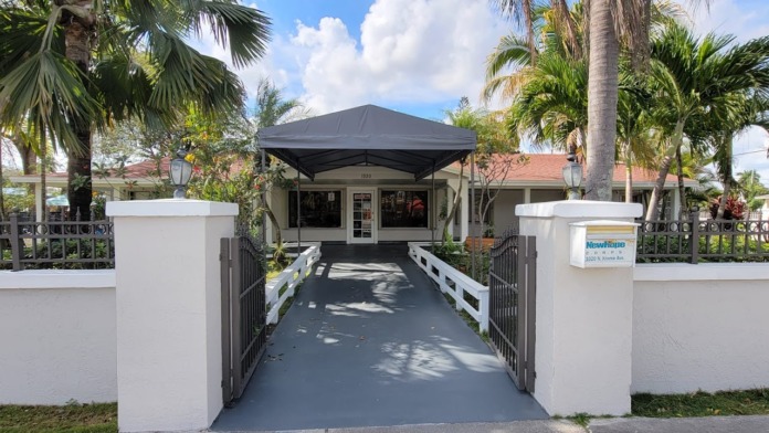 Exterior view of New Hope C.O.R.P.S. facility entrance with white columns, black awning, palm trees, and manicured landscaping