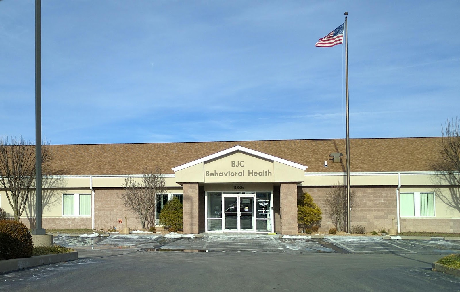 Exterior of BJC Behavioral Health facility showing main entrance with signage, parking area, and American flag
