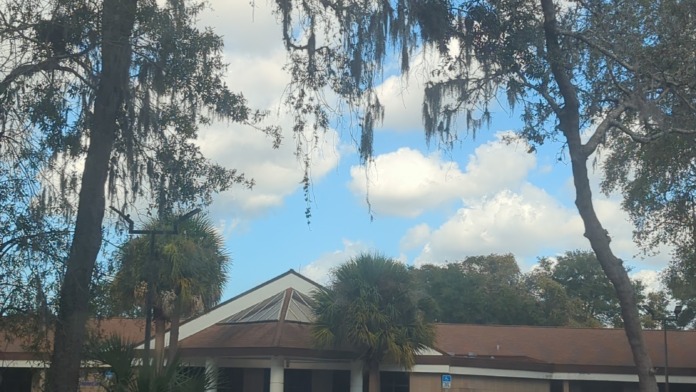 Exterior view of treatment center building with parking lot, parked vehicles, mature oak trees with Spanish moss, and clear sky