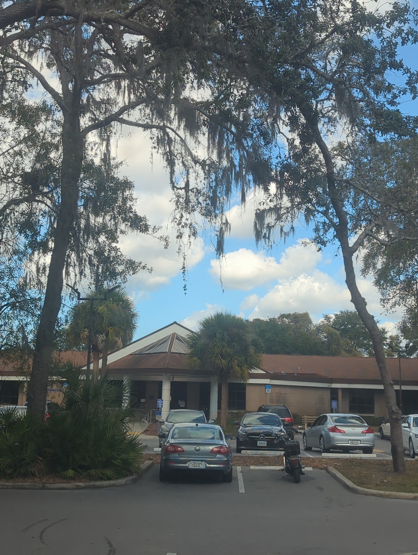 Exterior view of treatment center building with parking lot, parked vehicles, mature oak trees with Spanish moss, and clear sky