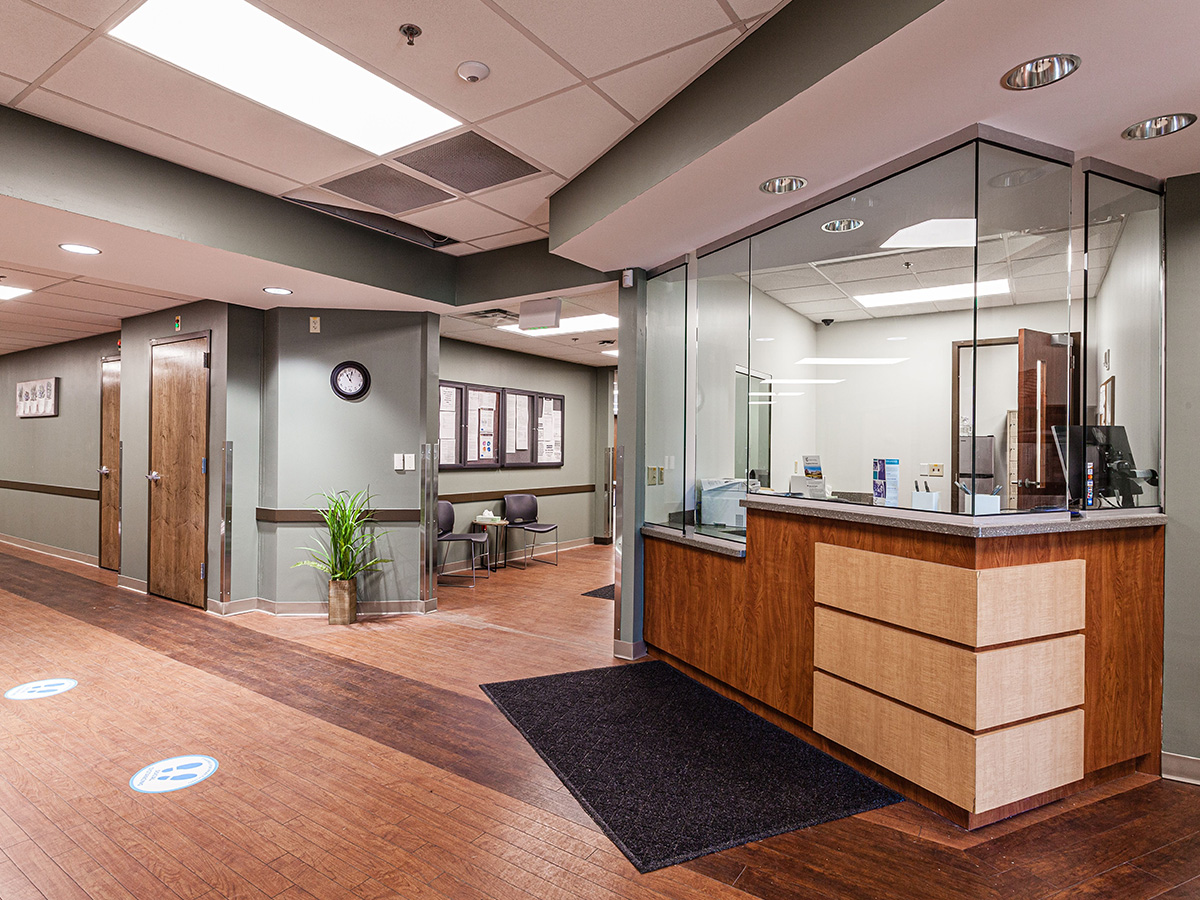 Interior reception lobby with wooden desk, glass partition, seating area, and professional check-in counter