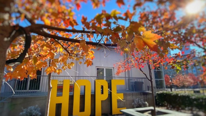 Outdoor area featuring large yellow HOPE letters, autumn foliage, picnic tables, and facility building backdrop