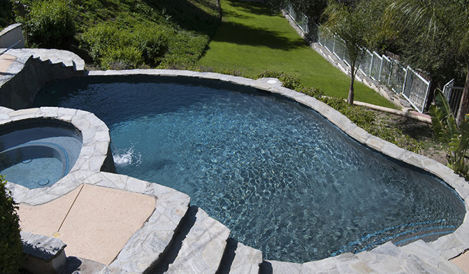 Exterior swimming pool and spa area surrounded by manicured grounds, landscaping, and white safety fencing