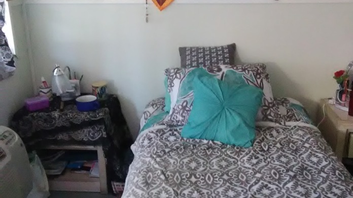Interior patient bedroom showing bed, small desk area, wall-mounted artwork display board with various creative pieces