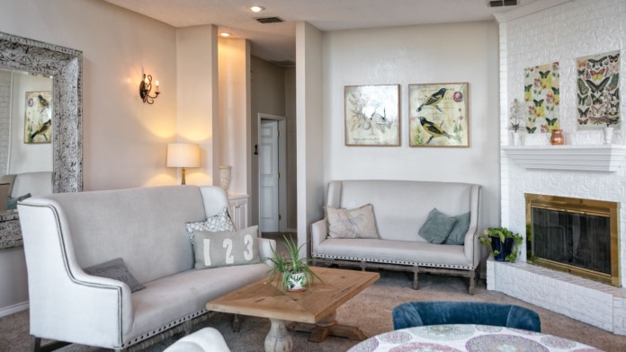 Interior lounge space with gray upholstered seating, fireplace with white brick, decorative wall art, and wooden coffee table
