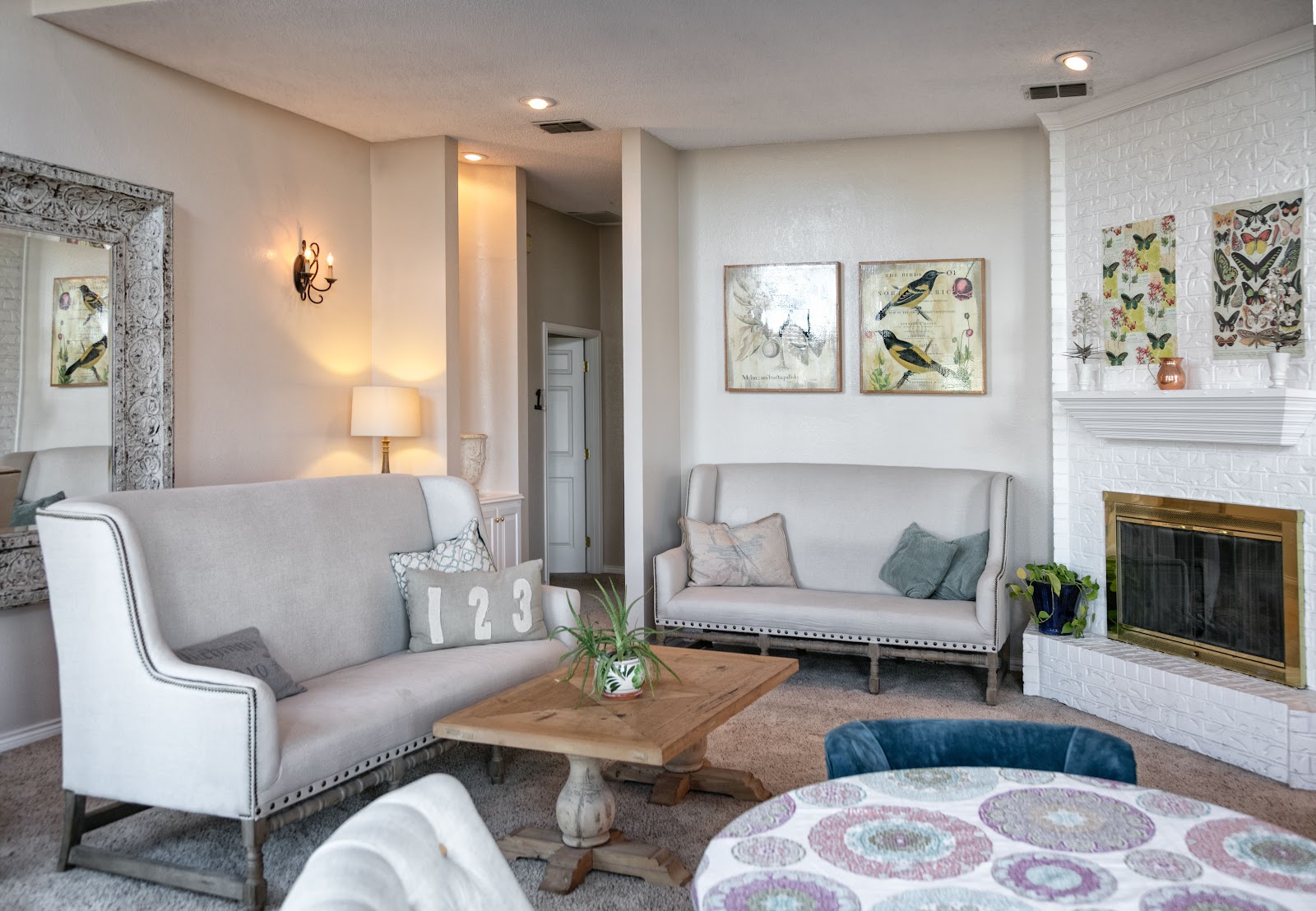 Interior lounge space with gray upholstered seating, fireplace with white brick, decorative wall art, and wooden coffee table