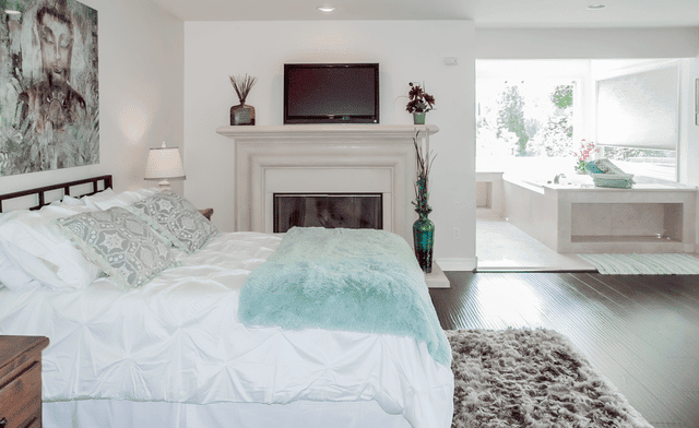 Interior bedroom with queen bed, fireplace, wall-mounted television, seating area, and ensuite bathroom