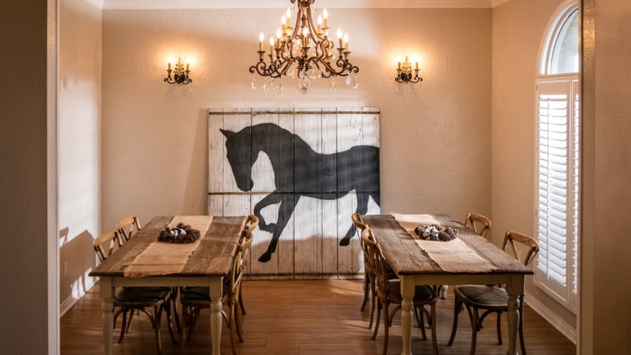 Interior dining space with two wooden tables, upholstered chairs, horse silhouette wall art, and decorative lighting