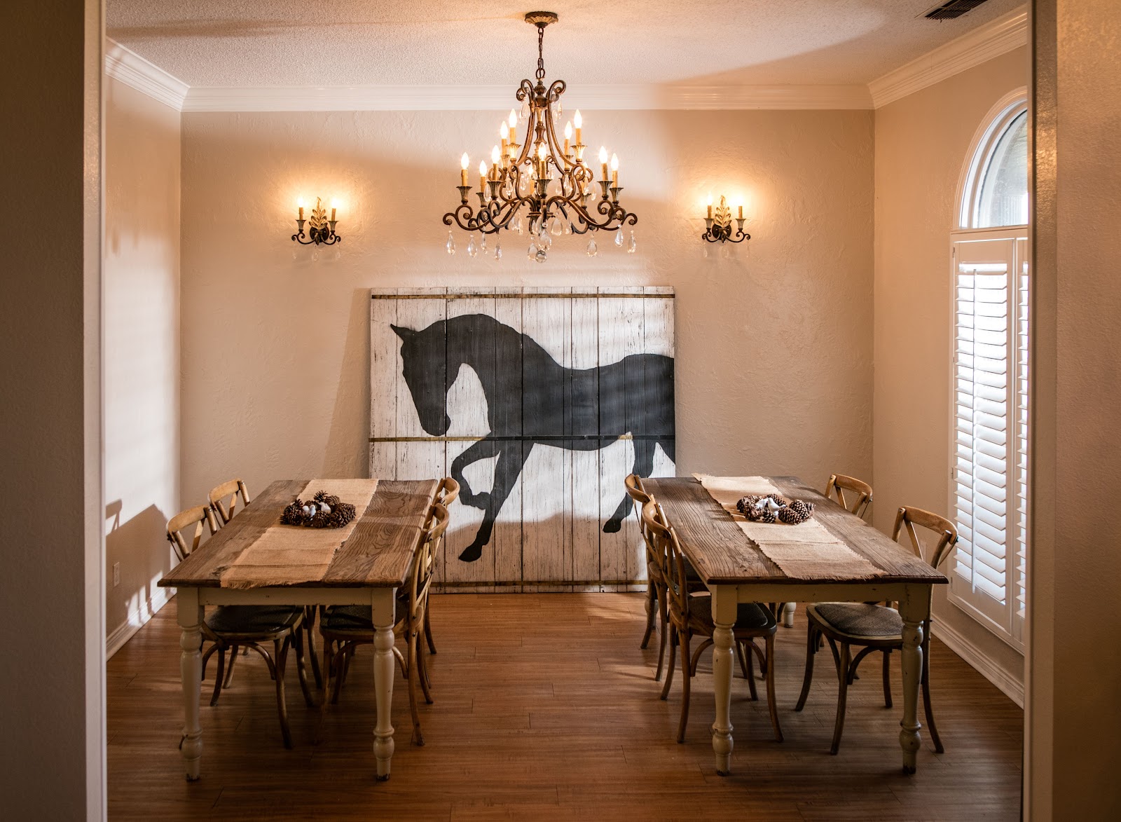 Interior dining space with two wooden tables, upholstered chairs, horse silhouette wall art, and decorative lighting