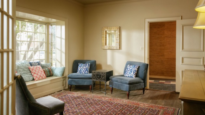Interior lounge with blue and gray upholstered chairs, window seat with cushions, decorative artwork, and hardwood flooring