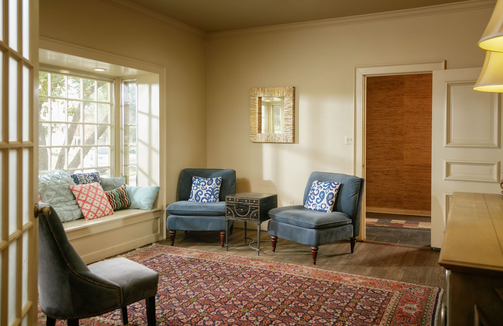 Interior lounge with blue and gray upholstered chairs, window seat with cushions, decorative artwork, and hardwood flooring