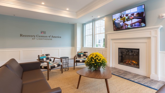 Interior reception area with comfortable seating, fireplace, and Recovery Centers of America at Lighthouse branding on accent wall