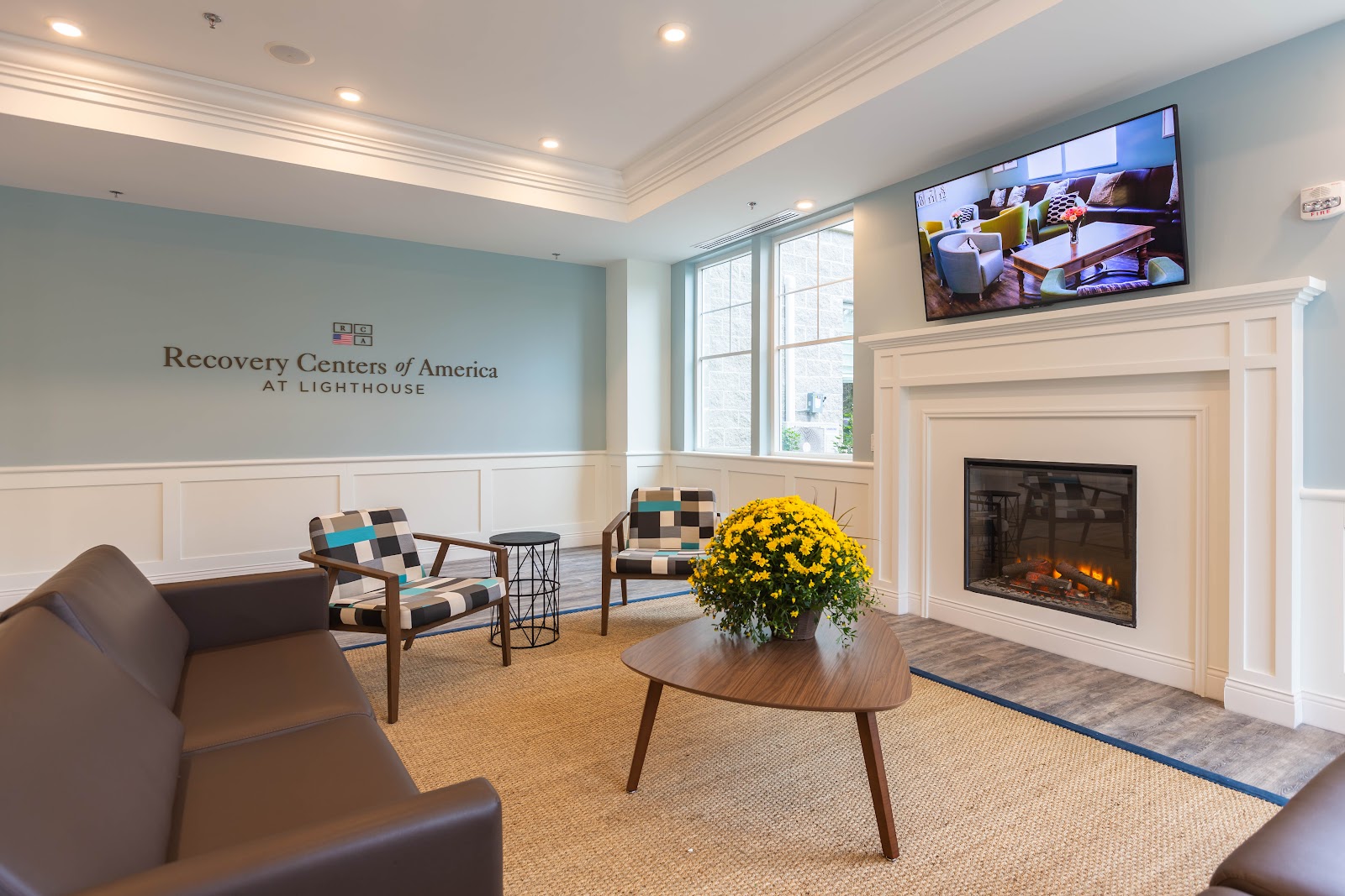 Interior reception area with comfortable seating, fireplace, and Recovery Centers of America at Lighthouse branding on accent wall