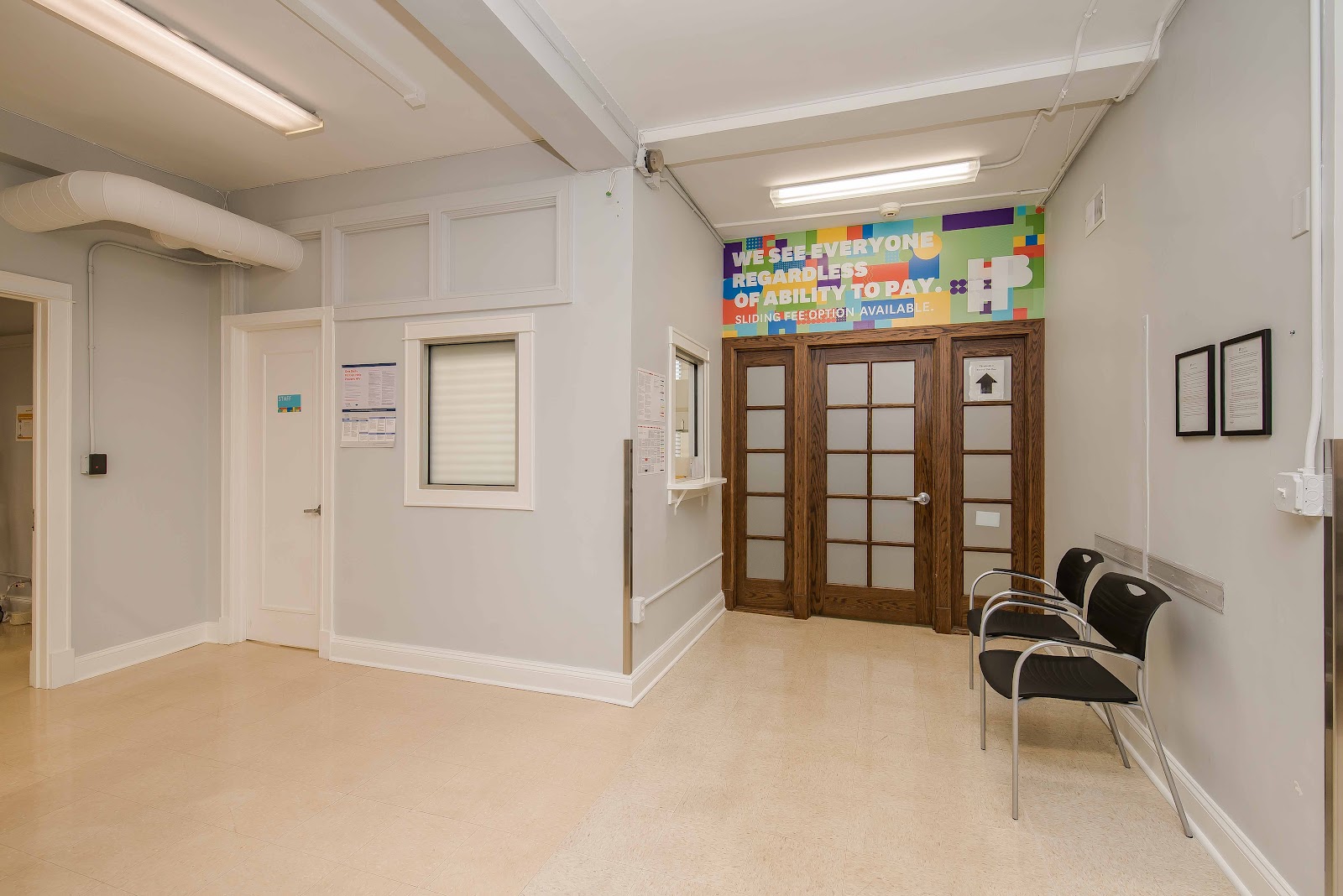 Interior reception space with colorful informational signage, wooden doors, chairs, exit sign, and administrative counter
