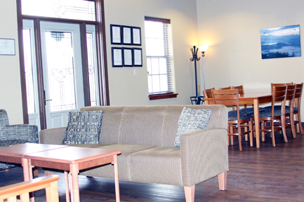 Interior recreation space with upholstered seating, small tables, wooden dining chairs, and warm ambient lighting