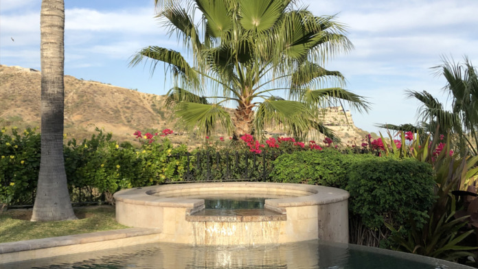 Outdoor spa or hot tub surrounded by tropical plants, palm trees, flowering shrubs, and mountain views