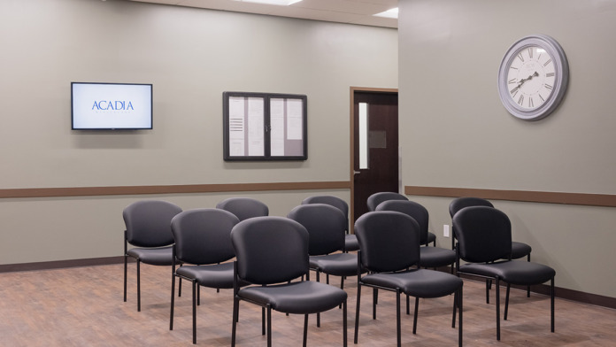 Interior Acadia program room with rows of black chairs, wall-mounted screen, wall clock, and professional setup