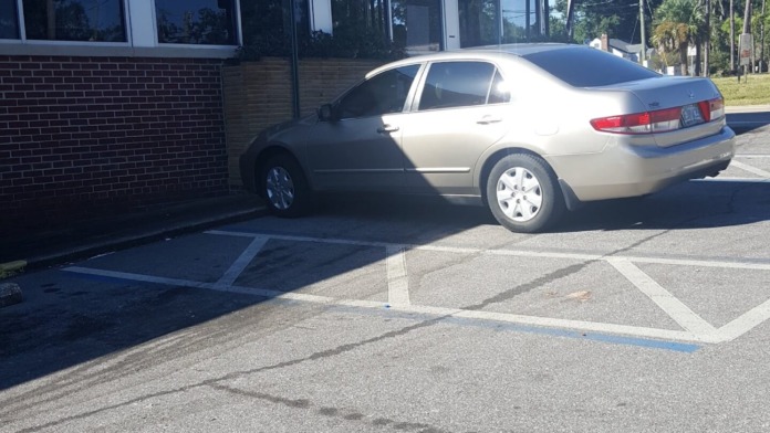 Exterior accessible parking space with wheelchair symbol marking, brick building facade with large windows, metal railings and canopy