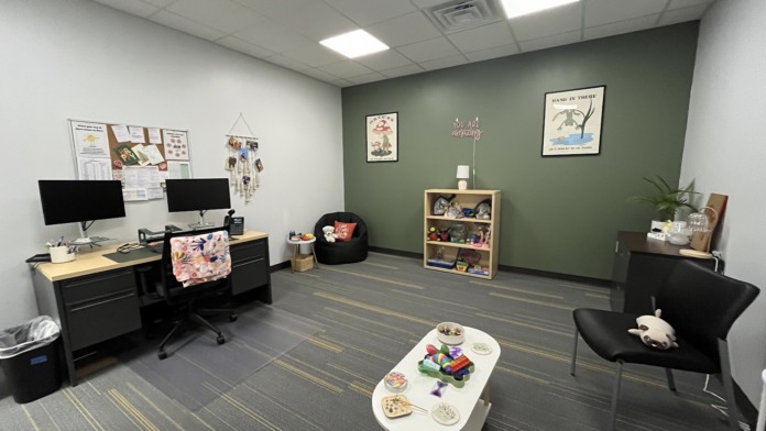 Interior activity space with colorful walls, computer stations, gaming supplies, shelving with toys and books, bean bag chairs