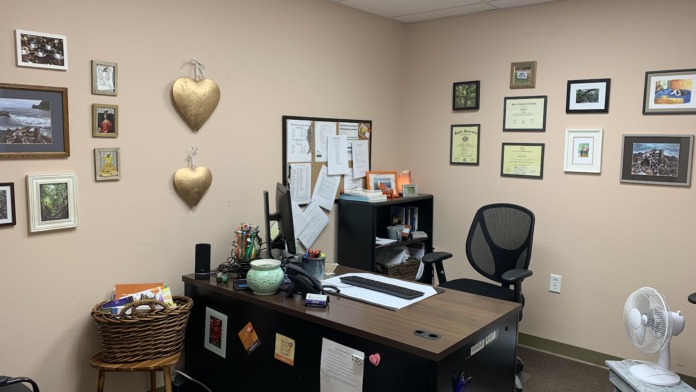 Interior office space with desk, office supplies, computer, black office chair, and walls decorated with framed pictures and documents