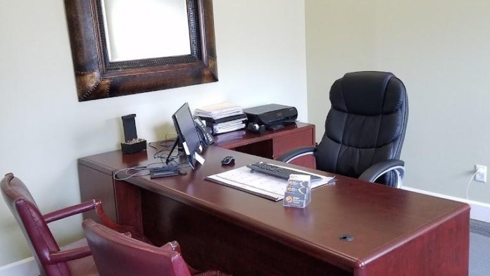 Interior office with wooden desk, burgundy leather chairs, framed mirror on wall, and professional workspace