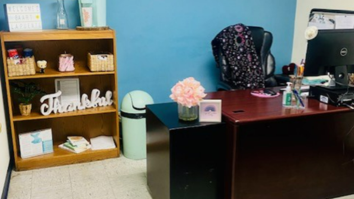 Interior office with bright blue accent wall, wooden shelving, desk, office chair, computer monitor, and organized supplies.