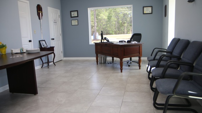 Interior office space with blue walls, wooden desk, office chairs, windows, and framed certifications