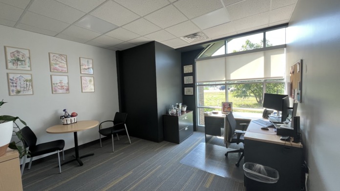 Interior office with desk, computer station, large windows overlooking outdoor area, accent wall, and workspace furnishings