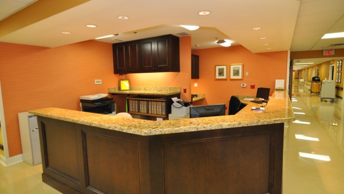 Interior reception desk with orange accent walls, granite countertop, dark cabinetry, and view of hallway corridor