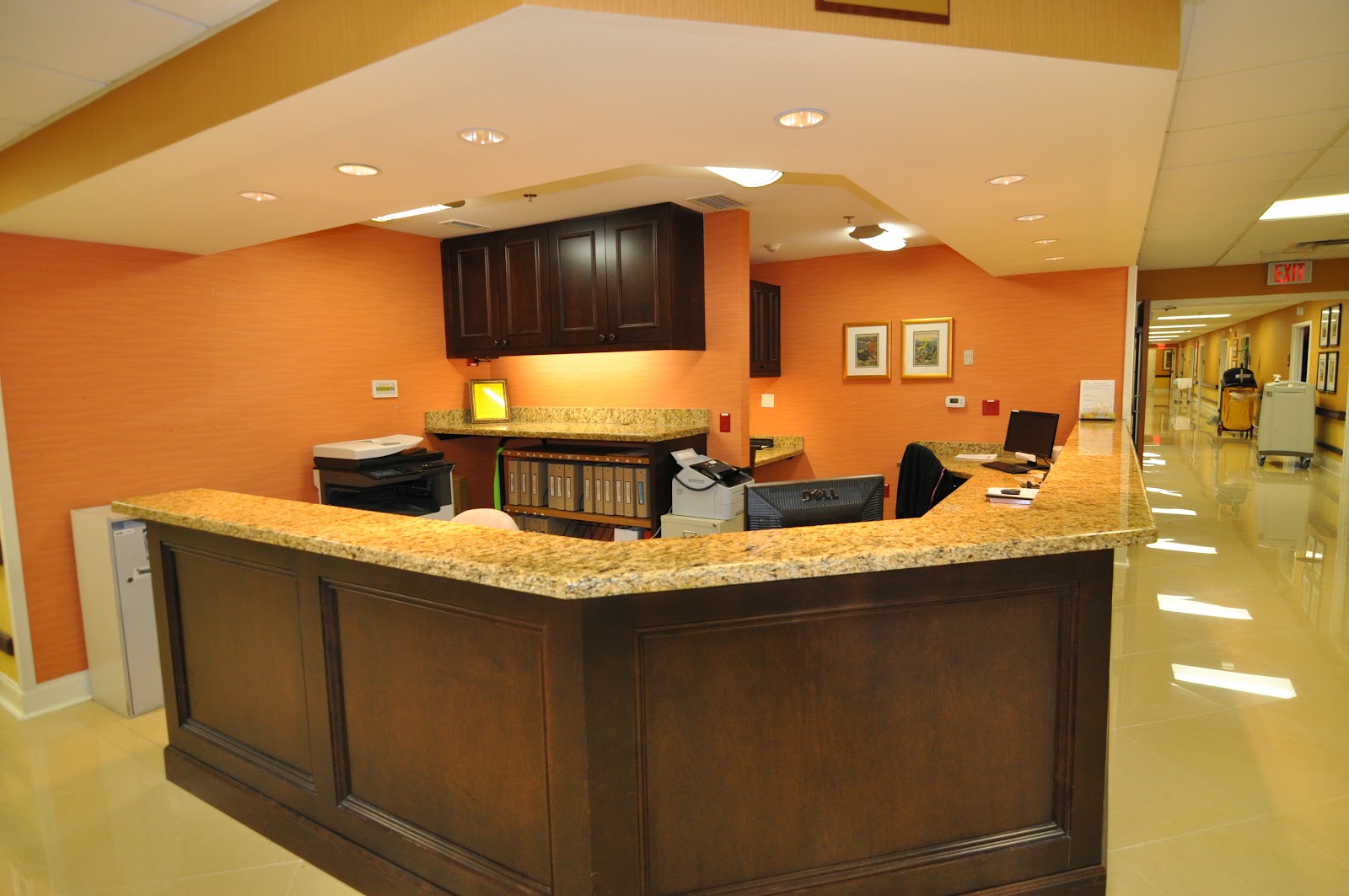 Interior reception desk with orange accent walls, granite countertop, dark cabinetry, and view of hallway corridor