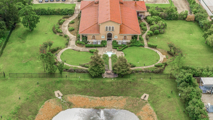 Aerial view of entire facility showing main building, manicured grounds, parking areas, pond, and surrounding landscape