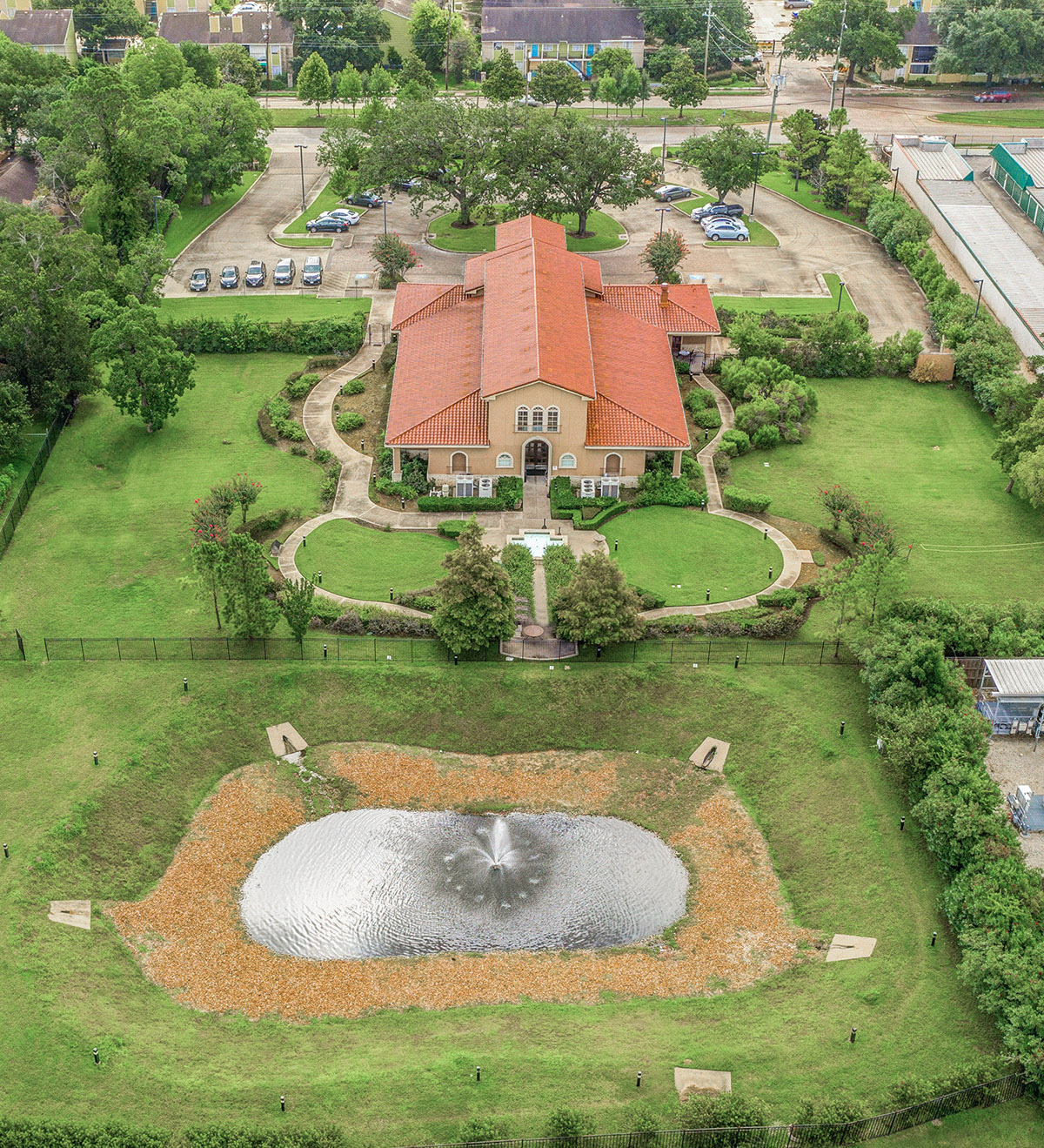 Aerial view of entire facility showing main building, manicured grounds, parking areas, pond, and surrounding landscape