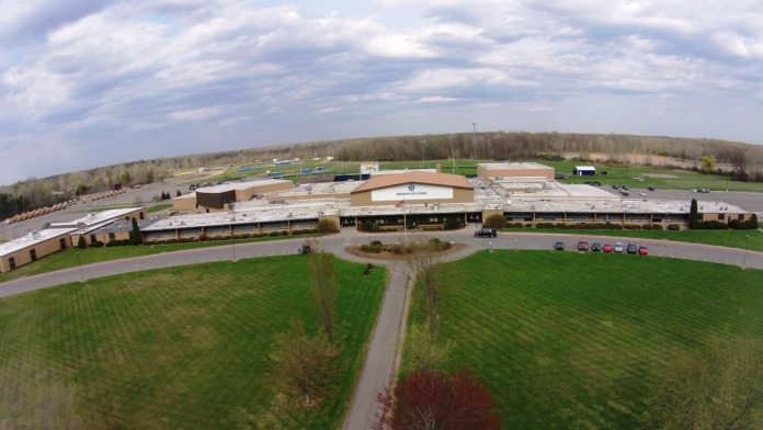 Aerial view of entire school campus showing brick building complex, parking areas, athletic fields, and surrounding grounds