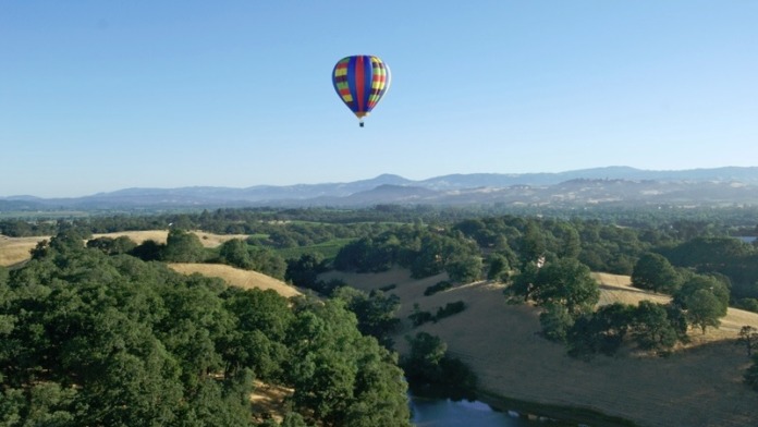Exterior aerial view of rural landscape with green fields, trees, water, and hot air balloon in sky