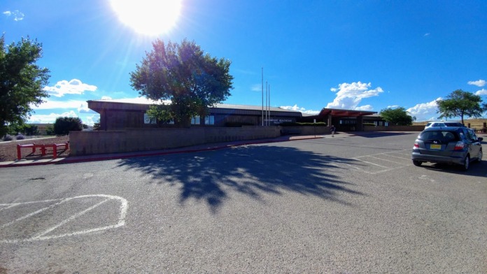 Exterior view of parking lot with vehicles, facility building with signage, landscaping, and trees