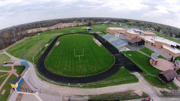 Aerial view of outdoor athletic facilities including football field with track, soccer fields, and sports equipment on school campus