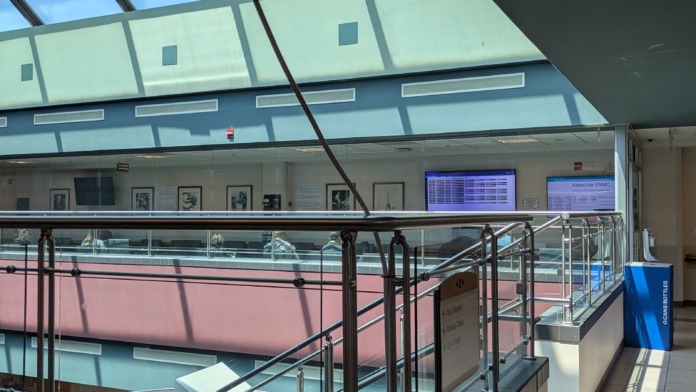Interior multi-level atrium featuring modern architectural design with geometric skylight, glass railings, metal support structures, and colored wall panels