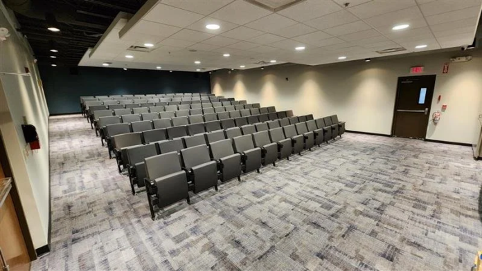 Interior auditorium with rows of gray theater seating, white ceiling, and exit signage