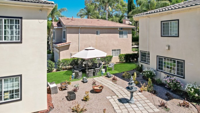 Outdoor patio with black gazebo, lounge seating, fountain features, and manicured lawn with landscaping